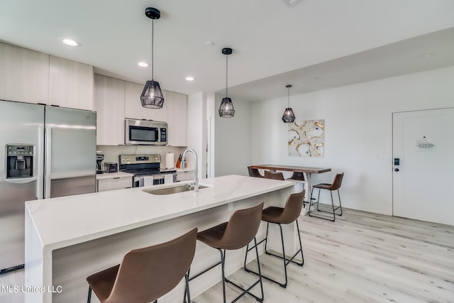 kitchen featuring appliances with stainless steel finishes, sink, light wood-type flooring, hanging light fixtures, and a kitchen island with sink