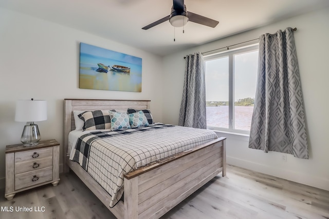 bedroom with a water view, hardwood / wood-style flooring, and ceiling fan