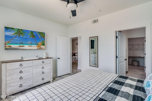 bedroom with a walk in closet, a closet, light wood-type flooring, and ceiling fan