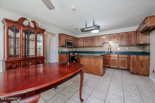 7488 Hickory Estates Dr, Walls, MS 38680 - kitchen with brown cabinetry, backsplash, dark countertops, appliances with stainless steel finishes, and light tile patterned floors