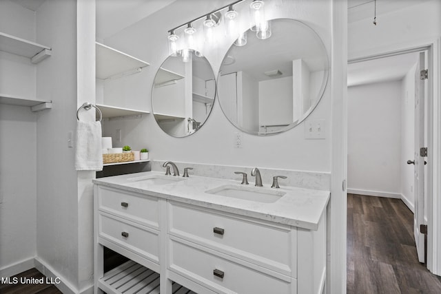 full bathroom featuring double vanity, baseboards, a sink, and wood finished floors