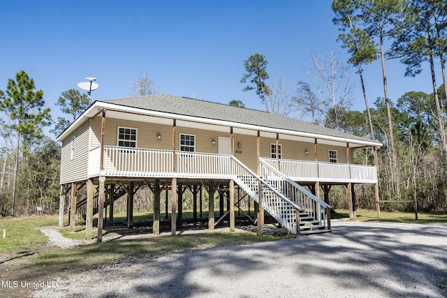 coastal home with covered porch, a shingled roof, stairs, and a carport