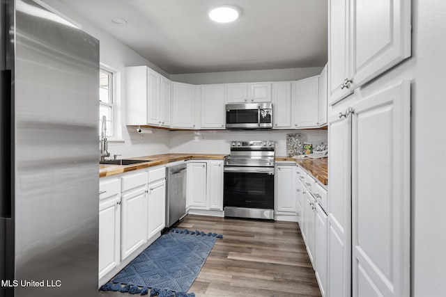 kitchen featuring stainless steel appliances, butcher block counters, white cabinetry, and backsplash