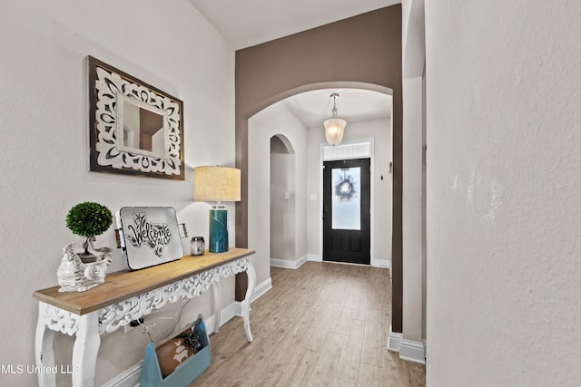 foyer with arched walkways, baseboards, and wood finished floors