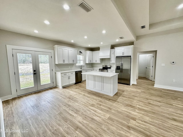 kitchen featuring stainless steel appliances, a center island, premium range hood, sink, and white cabinetry