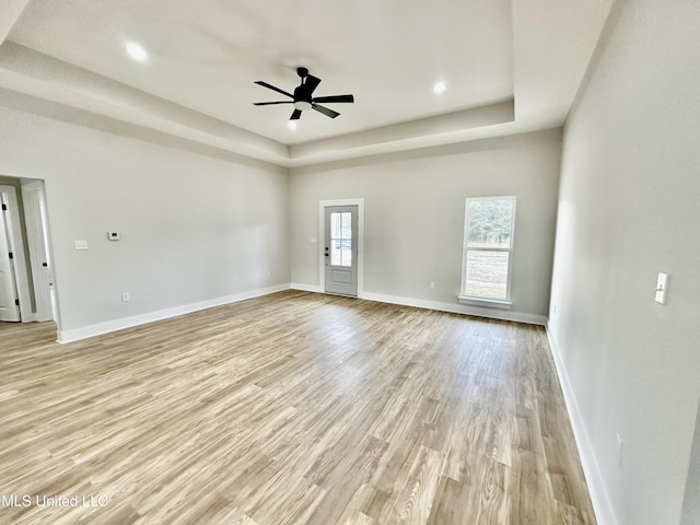 unfurnished living room with light hardwood / wood-style floors, ceiling fan, and a raised ceiling