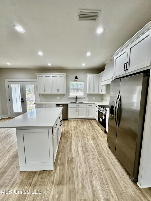 kitchen with appliances with stainless steel finishes, white cabinetry, sink, and premium range hood