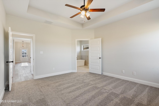 unfurnished bedroom with ensuite bathroom, baseboards, visible vents, a tray ceiling, and light colored carpet