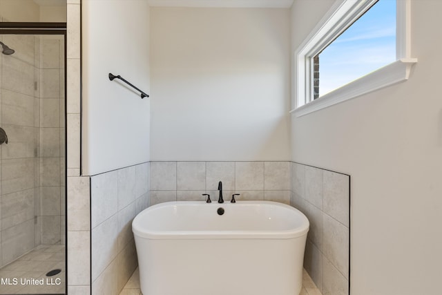 bathroom with tile walls, a freestanding tub, and a stall shower