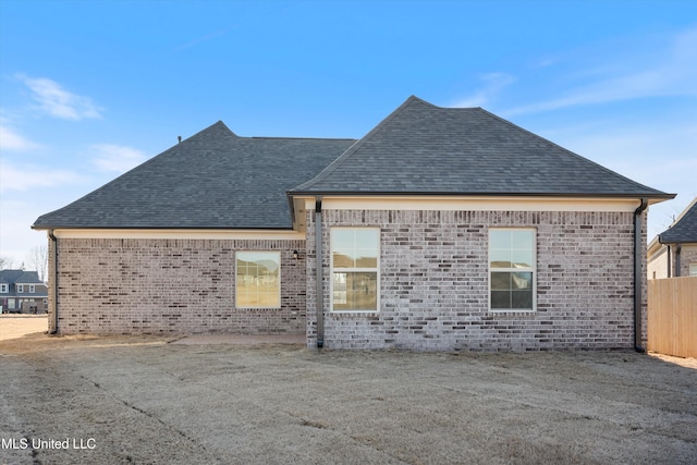 rear view of property featuring a shingled roof, fence, and brick siding