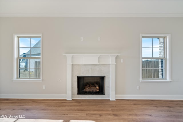 unfurnished living room with a wealth of natural light, a tile fireplace, crown molding, and wood finished floors