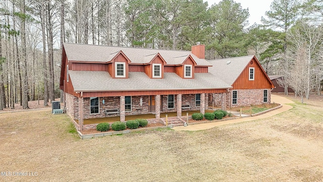 view of front facade featuring a front yard, a chimney, a porch, and brick siding