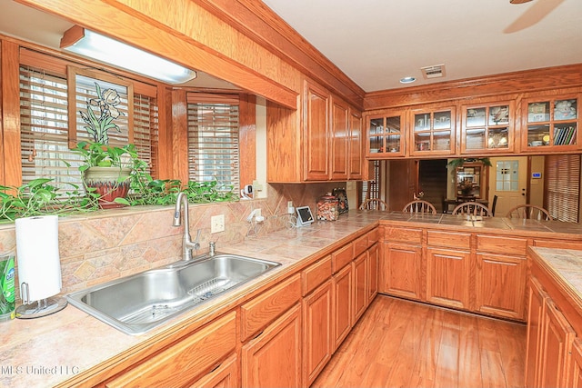 kitchen with light wood finished floors, tile counters, tasteful backsplash, glass insert cabinets, and a sink