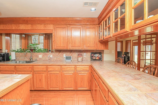 kitchen featuring glass insert cabinets, a sink, visible vents, and decorative backsplash