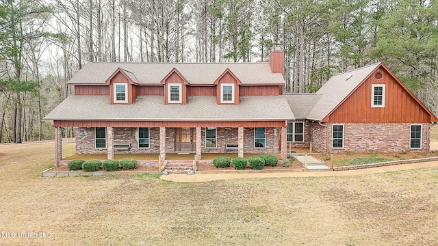 view of front of home featuring a shingled roof, a chimney, a front yard, a porch, and brick siding