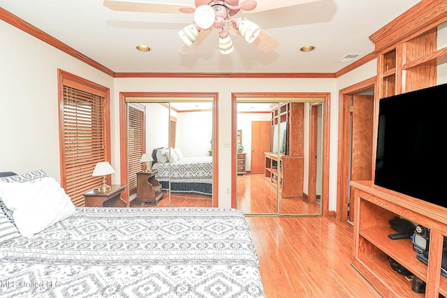 bedroom with crown molding, two closets, visible vents, light wood-style flooring, and a ceiling fan