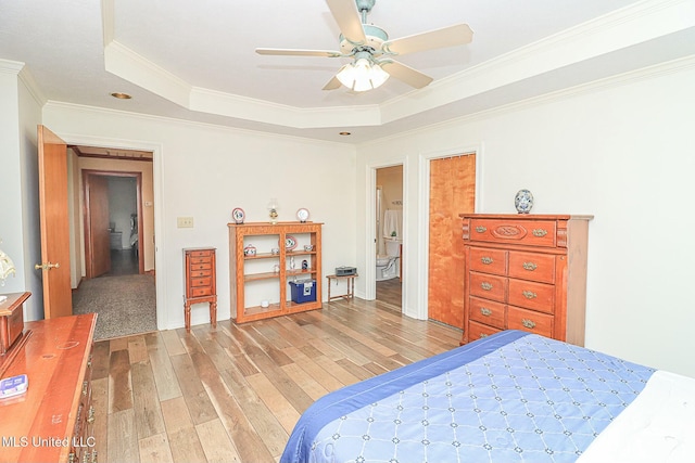 bedroom featuring a ceiling fan, light wood-style flooring, a tray ceiling, and crown molding