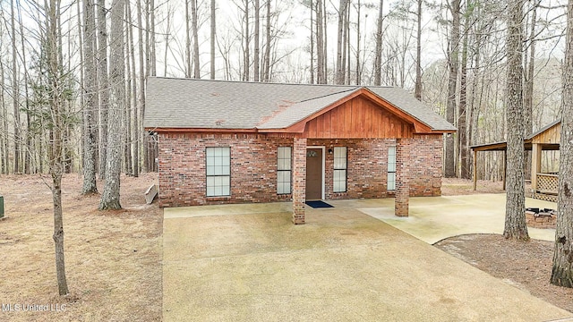 view of front of house with a patio area, brick siding, and roof with shingles