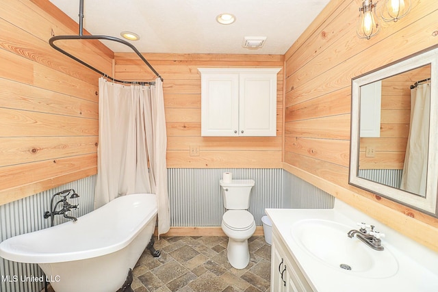 full bathroom featuring toilet, stone finish flooring, wood walls, vanity, and a freestanding tub