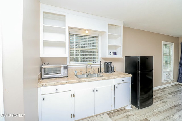 kitchen featuring open shelves, light countertops, freestanding refrigerator, a sink, and light wood-type flooring