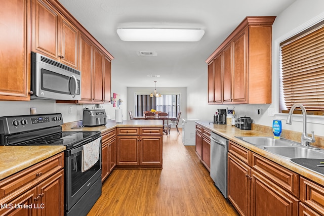 kitchen featuring stainless steel appliances, sink, hanging light fixtures, a chandelier, and light hardwood / wood-style flooring