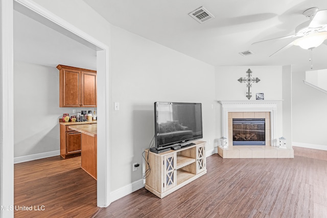 living room with dark hardwood / wood-style flooring, a tiled fireplace, and ceiling fan