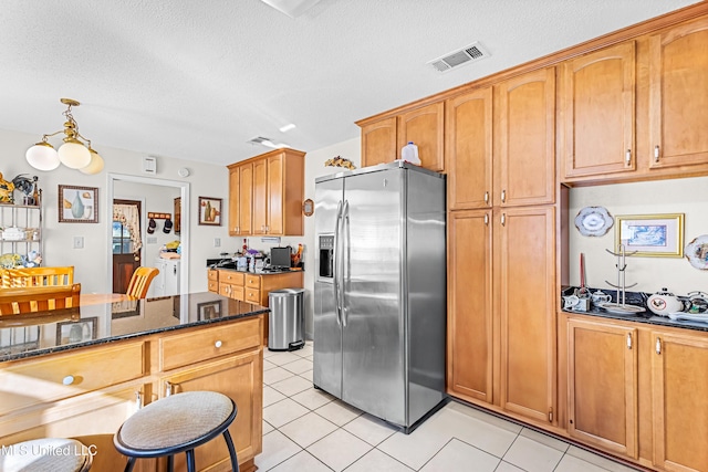 kitchen with stainless steel fridge with ice dispenser, a textured ceiling, decorative light fixtures, and dark stone counters