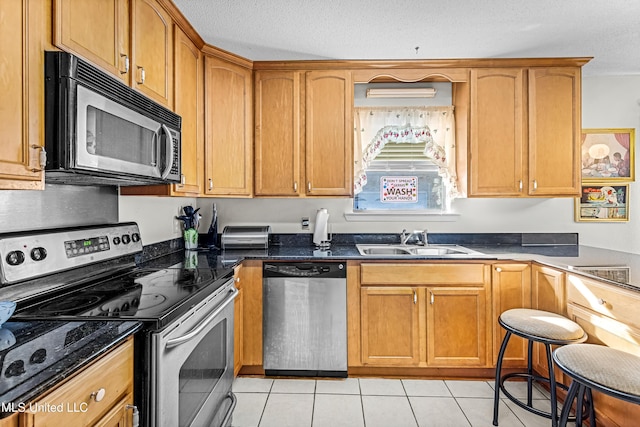 kitchen featuring appliances with stainless steel finishes, dark stone counters, a textured ceiling, sink, and light tile patterned floors