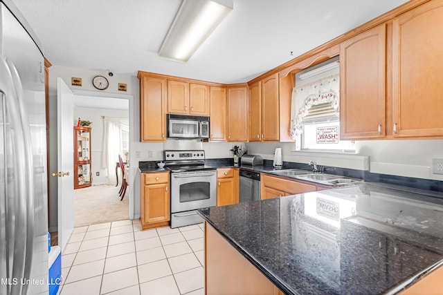 kitchen featuring light tile patterned flooring, appliances with stainless steel finishes, dark stone countertops, and sink