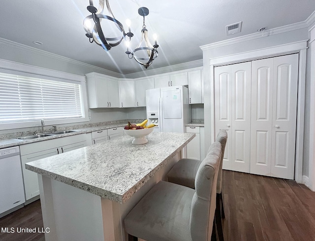 kitchen featuring white appliances, sink, a center island, hanging light fixtures, and white cabinetry