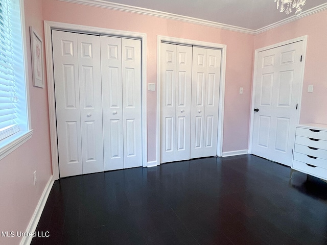 unfurnished bedroom featuring multiple closets, crown molding, and a chandelier