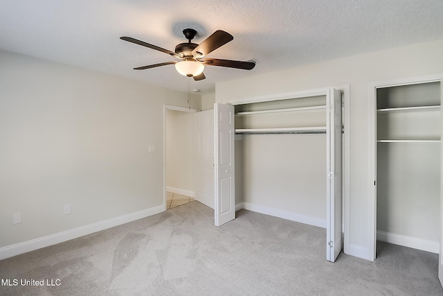 unfurnished bedroom with ceiling fan, light colored carpet, a textured ceiling, and two closets