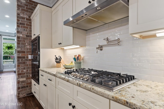 802 Old Spanish Trl, Bay Saint Louis, MS 39520 - kitchen featuring under cabinet range hood, stainless steel gas cooktop, black oven, dark wood finished floors, and white cabinetry