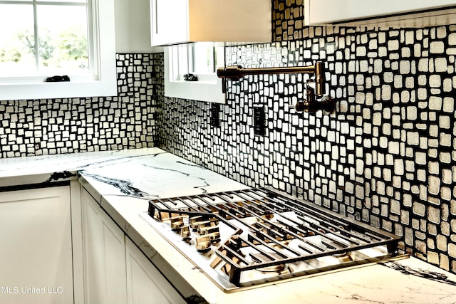 kitchen with stainless steel gas cooktop, light stone countertops, backsplash, and white cabinets