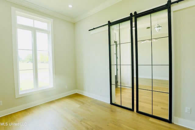 spare room with a wealth of natural light, ornamental molding, light hardwood / wood-style flooring, and a barn door