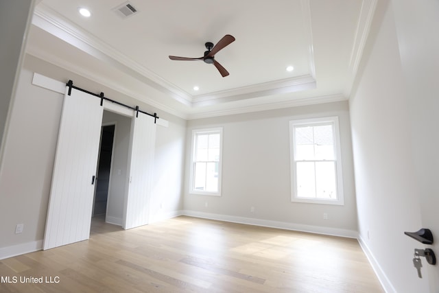 unfurnished bedroom featuring a tray ceiling, crown molding, a barn door, light hardwood / wood-style floors, and ceiling fan