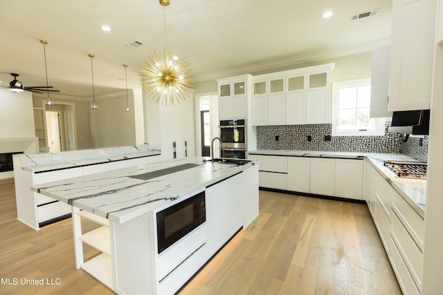 kitchen with stainless steel appliances, decorative light fixtures, light wood-type flooring, and white cabinets