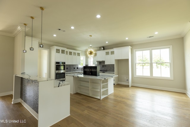 kitchen featuring kitchen peninsula, white cabinets, hanging light fixtures, light hardwood / wood-style floors, and light stone counters