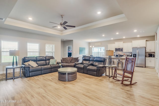 living room featuring ceiling fan with notable chandelier, a raised ceiling, light hardwood / wood-style flooring, and ornamental molding