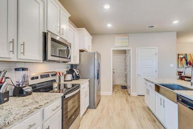 kitchen with stainless steel appliances, light stone countertops, light hardwood / wood-style flooring, white cabinets, and decorative backsplash