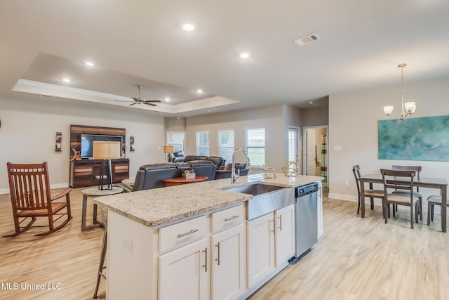 kitchen with a center island with sink, sink, stainless steel dishwasher, hanging light fixtures, and white cabinets