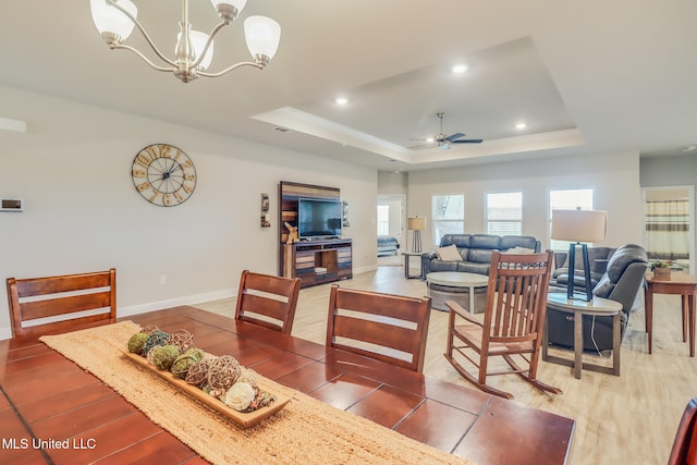 dining room featuring wood-type flooring, ceiling fan with notable chandelier, and a tray ceiling