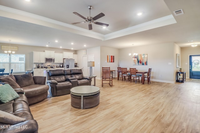 living room with ceiling fan with notable chandelier, a raised ceiling, crown molding, and light hardwood / wood-style flooring