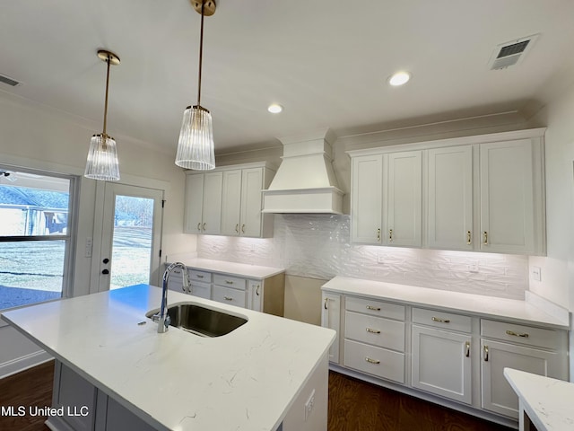 kitchen with white cabinetry, custom range hood, sink, and a center island with sink