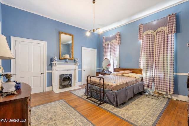 bedroom with crown molding, baseboards, wood finished floors, and a fireplace with flush hearth