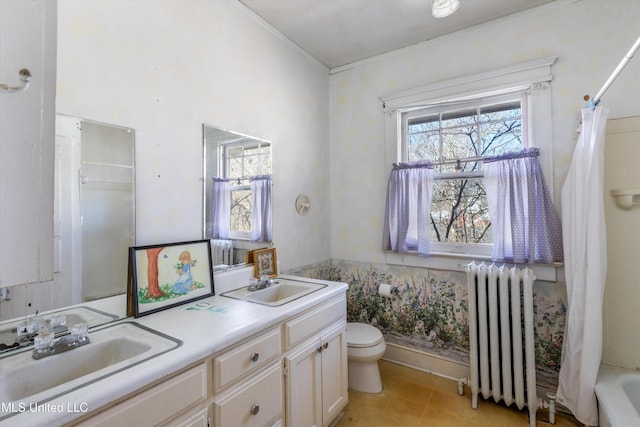 bathroom featuring double vanity, radiator heating unit, toilet, and a sink