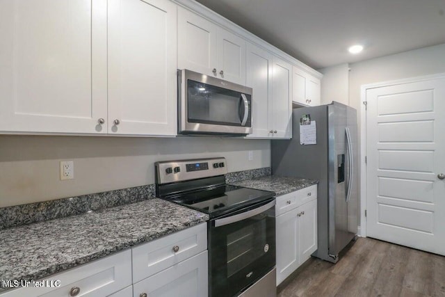 kitchen with white cabinets, appliances with stainless steel finishes, stone countertops, and wood-type flooring