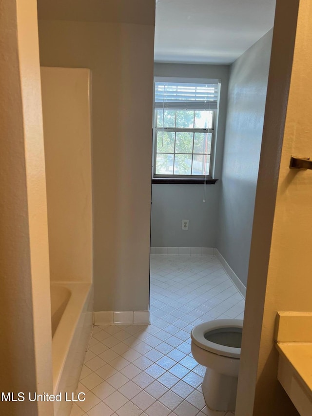 bathroom featuring tile patterned flooring, a tub, and toilet