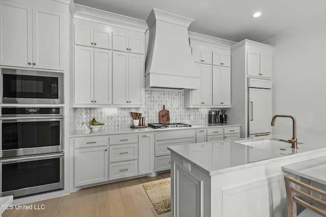 kitchen featuring tasteful backsplash, built in appliances, custom range hood, and a sink