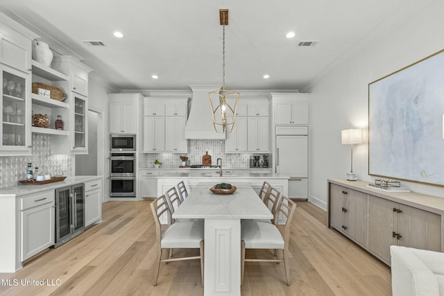 kitchen featuring beverage cooler, visible vents, custom exhaust hood, built in appliances, and a center island